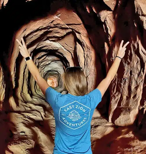 Person in a blue t-shirt stands in a tunnel, raising both hands in a peace sign.